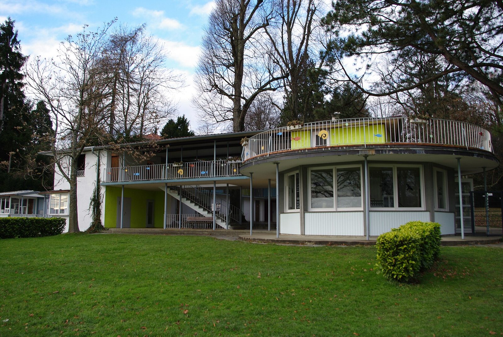 Das flache Hauptgebäude des Lindenhofbads in Lindau-Bad Schachen zwischen alten Bäumen