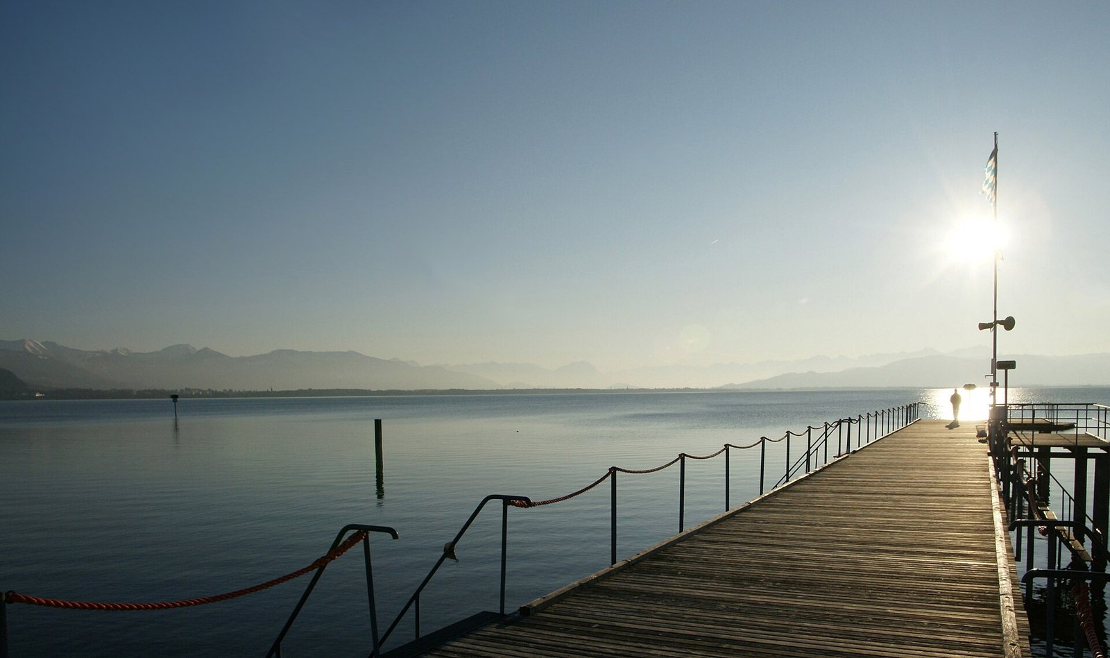 Holzsteg eines Strandbads in Lindau im Gegenlicht über dem ruhigen Bodensee