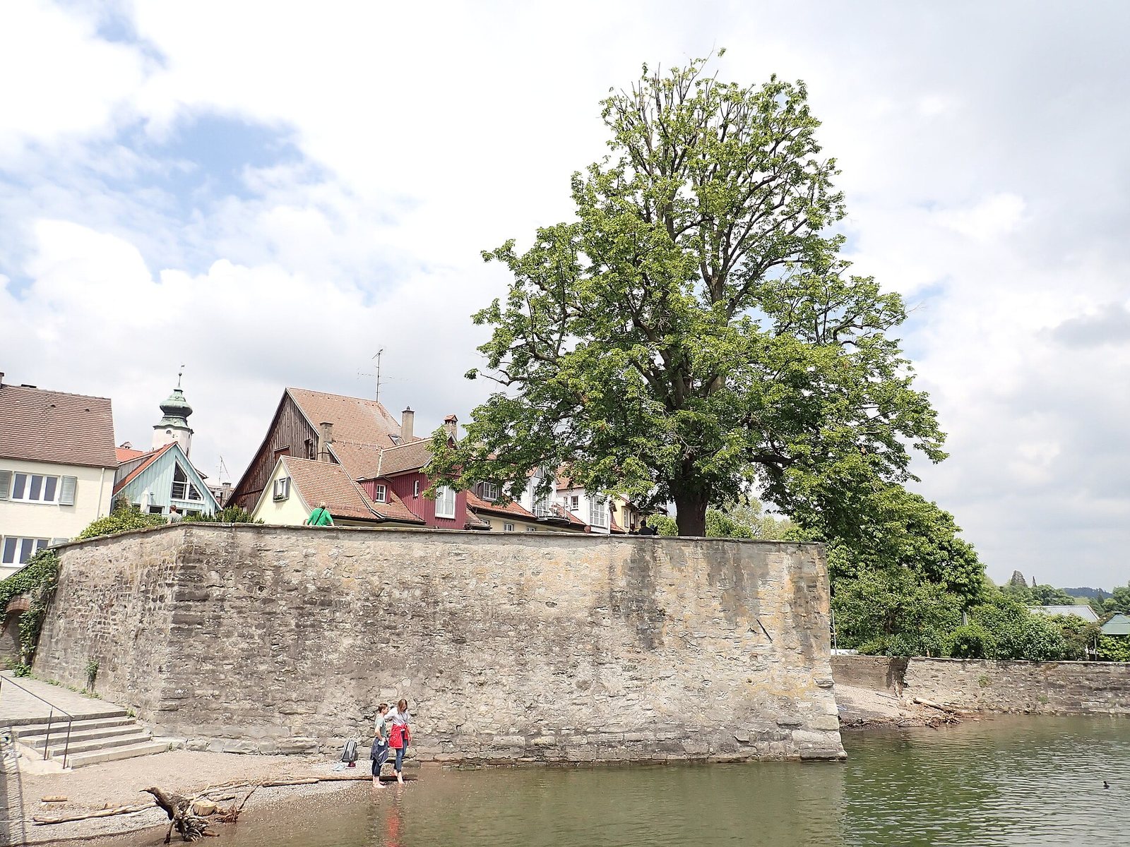Die steinerne Gerberschanze ragt in den Bodensee, davor Menschen im flachen Wasser