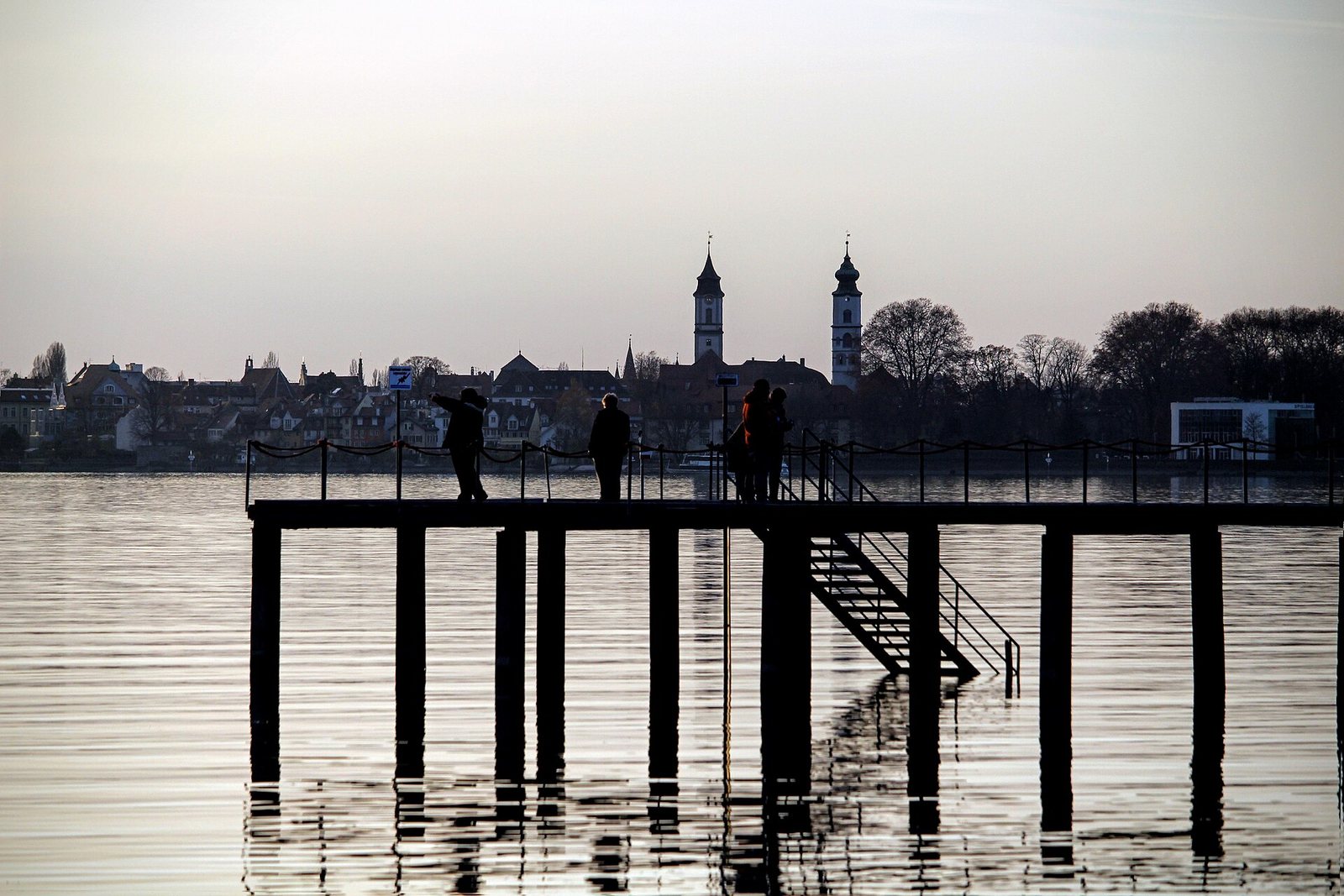 Silhouette der Insel Lindau mit Kirchtürmen hinter einem Steg im Gegenlicht
